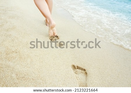 Beach travel - woman relaxing walking on a sandy beach leaving footprints in the sand. Close up detail of female feet on golden sand at a beach in Greece. Background.