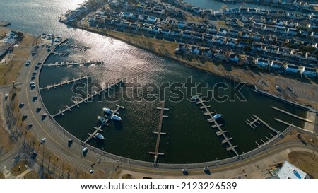 An aerial shot over a marina in the shape of semicircle, taken on a sunny day on Long Island, NY. There are many floating piers but only a few boats in the water.