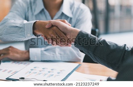 businesspeople are shaking their hands after signing a contract, while standing together in a sunny modern office, close-up. Business communication, handshake, and marketing concept