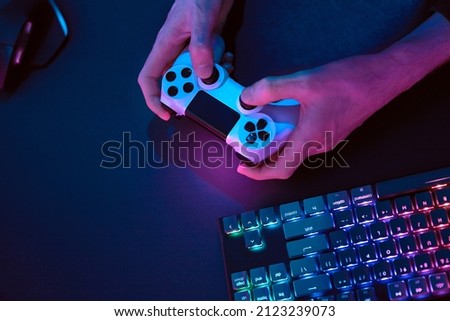 Male hands using controller for controlling computer. Rainbow colors backlighted gaming computer keyboard. Professional computer game playing, esport business and online world concept. Royalty-Free Stock Photo #2123239073
