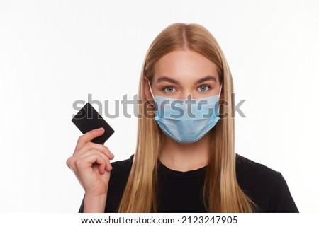 woman with credit card wearing a medical mask isolated on a white background. Conceptual photo, purchases with cashless payment during quarantine.