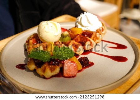 the waffle cake on top with vanilla ice cream, fresh fruit (kiwi raspberry peppermint) and strawberry sauce on circle plate