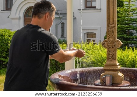 a man put his hands under a stream of water on a hot sunny day. background picture.