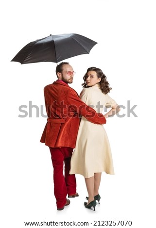 Walks. Young family couple, man and woman in retro style clothes, fashion of 70s, 60s years walking with umbrella isolated on white background. Concept of emotions, relationship, beauty.
