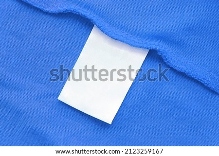 Blank white laundry care clothes label on blue fabric texture background.