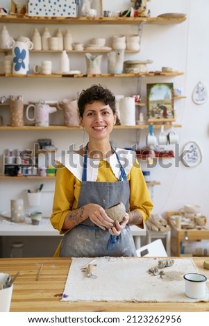 Portrait of happy smiling self-employed pottery artist in creative studio working with raw clay shaping handmade cup or jar. Cheerful ceramics art teacher recording master class lesson in workshop