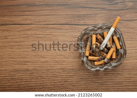 Glass ashtray with cigarette stubs on wooden table, top view. Space for text