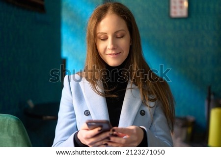 Beautiful young business woman smiling, using phone in a colorful cafe restaurant.