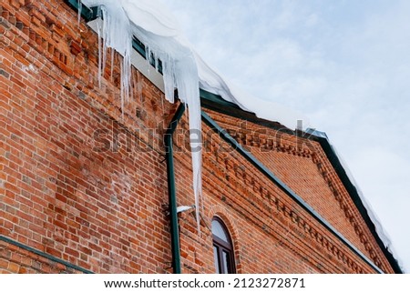 A huge icicle hangs from the roof of a brick building. Dangerous and sharp icicles on the facade of the house. Be careful in winter.natural phenomena. High quality photo