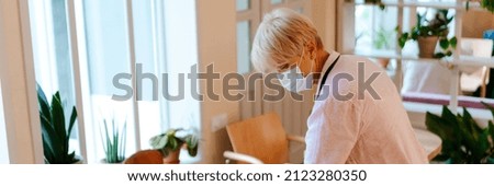 Mature woman wearing face mask using measuring tape while working in cafe