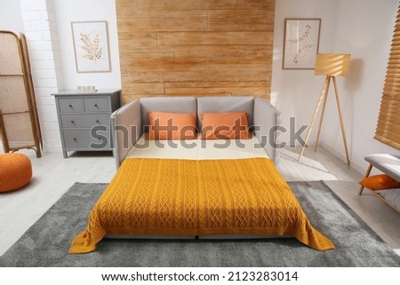 Room interior with sofa unfolded into bed near wooden wall Royalty-Free Stock Photo #2123283014