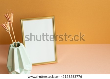 Blank photo frame with vase of dry flowers on pink table. orange wall background. copy space