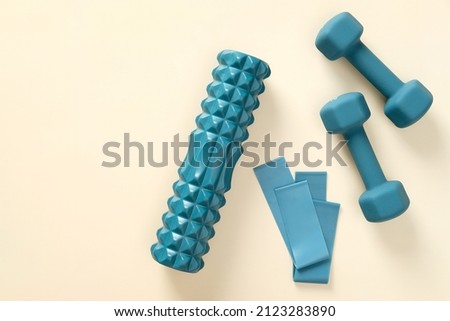 Blue workout equipment set on beige background. Dumbbells, fitness tape, roller. Flat lay, top view. Royalty-Free Stock Photo #2123283890