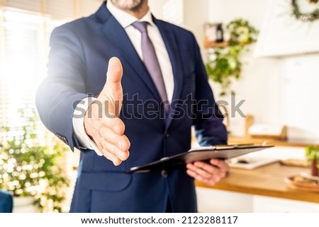 Conceptual photo of real estate or insurance agent with documents file. Man shakes the hand to the camera. 