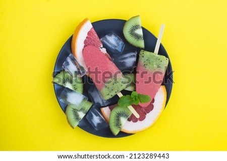 Top view of popsicles with kiwi and grapefruit on the black plate on the yellow background. Copy space.