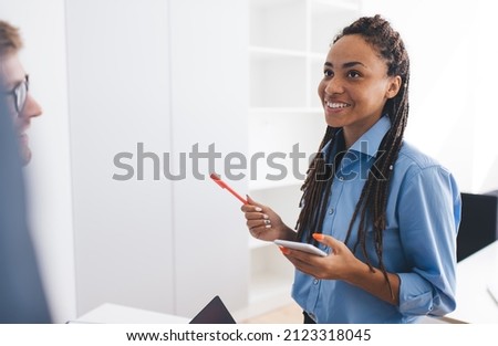 Happy African American female employee with smartphone gadget communicate with colleagues enjoying time for together briefing in office interior, cheerful woman with cellphone discussing business Royalty-Free Stock Photo #2123318045