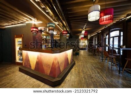 Modern interior of cafe with wooden counter and comfortable chairs at tables under glowing chandeliers