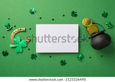 Top view photo of the white paper card bronze horseshoe and a lot of confetti in shape of clovers dots hats and black pot with coins on the green isolated background blank space