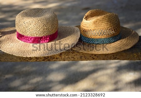 Two old straw hats, one for a woman and one for a man, lie side by side on a wooden bench in the shade, with space for text underneath Royalty-Free Stock Photo #2123328692