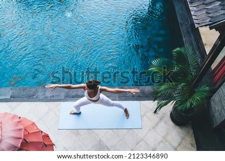 Top view of woman in track suit stretching in yoga pose breathing - enjoying recreation at patio pool terrace, Caucasian female practice yoga feeling balance in asana keeping body shape in tonus