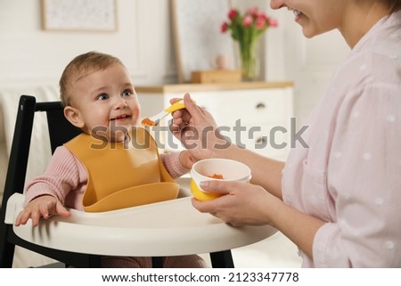 Mother feeding her little baby at home. Kid wearing silicone bib Royalty-Free Stock Photo #2123347778