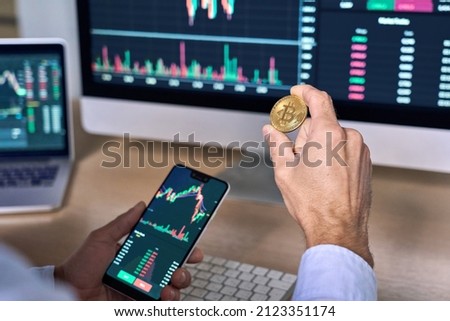 Business man crypto trader investor analyst holding smartphone and gold bitcoin coin buying cryptocurrency tokens analyzing stock market data investment risks using online trading mobile app concept. Royalty-Free Stock Photo #2123351174