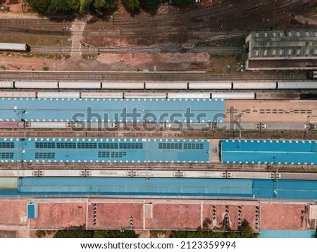 drone shot aerial view top angle bright sunny day beautiful town railway line track trains carriages compartments blue platform roof 