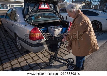Senior woman folding rollator at car trunk