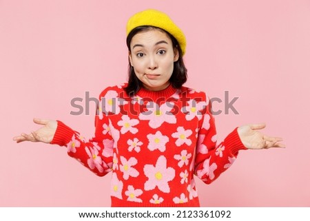 Uncertain woman of Asian ethnicity 20s wear red knitted sweater beret shrugging shoulders looking puzzled, have no idea isolated on plain pastel pink background studio People lifestyle fashion concept