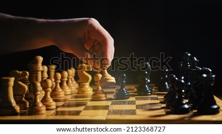 Player hand with a chess piece in a board game. Opening of the chess game, copy space on a black background