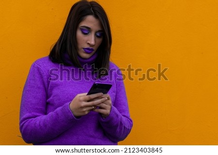 portrait of a woman in purple dress and make-up chatting with a cell phone on a yellow background
