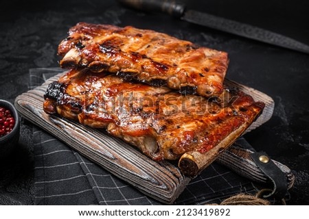 Stack of grilled pork ribs in BBQ sauce on a chopping board. Black background. Top view Royalty-Free Stock Photo #2123419892