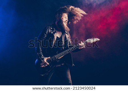 Emotional expressive man rock guitar player with long hair and beard plays on the black background. Smoke background. Studio shot.  Royalty-Free Stock Photo #2123450024