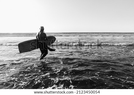 Surfer senior man having fun while surfing on beach with vintage surf board - Focus on male back - Black and white edition
