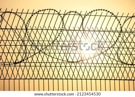 Barbed wire wall against the backdrop of the setting sun. The metaphor of slavery and the search for freedom. Restricted area. Border line of the territory
