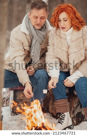 A couple in love, a man and a woman in a winter forest around a campfire drink coffee and give marshmallows. High quality photo