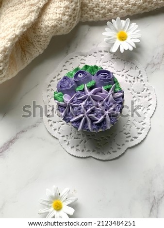 Top view of purple cupcakes decorated with floral theme on white blurry background with some shadow.