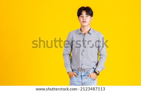 Studio shot of millennial Asian young male fashion model in stylish fashionable casual outfit standing on yellow background