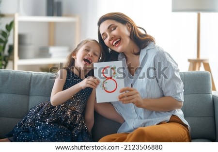 Happy International Women's Day! Child daughter is congratulating mother and giving her postcard. Mum and girl smiling and hugging. Family holiday and togetherness.