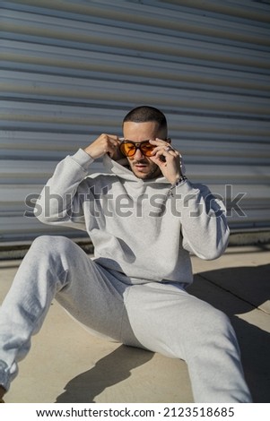 A vertical shot of a cool stylish young male with orange sunglasses and a gray sweatsuit posing Royalty-Free Stock Photo #2123518685