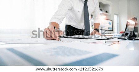 Young businessman writing business plan at desk in modern office. Planning analyze investment, business strategy and marketing, using graph chart and digital tablet.