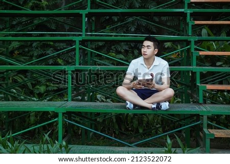 student boy with white shirt, blue short is studying in green park