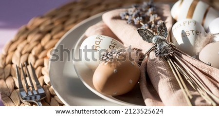 Banner. Table setting. A plate with a rabbit on a napkin, lavender and Easter eggs on a fashionable background of 2022 is a veri pery. Top view. The concept of a happy Easter holiday for cafes. Royalty-Free Stock Photo #2123525624