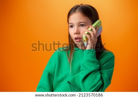 Teen girl talking on cell phone isolated on orange background