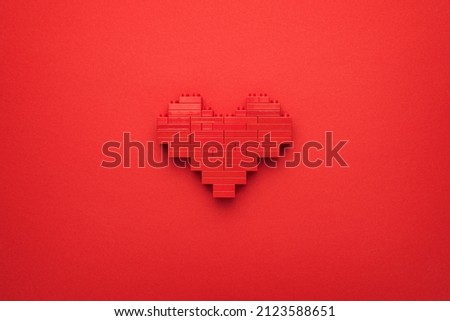 Red heart symbol made of plastic building blocks. Flat lay image of like button on red background. Top-down composition of toy pixelated heart model. Minimalist photo of stylized red love symbol.