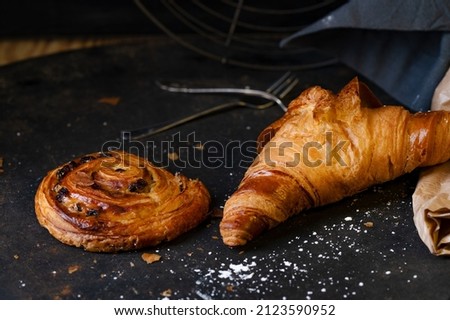 A closeup shot of a croissant and a cinnamon roll on a dark grey table