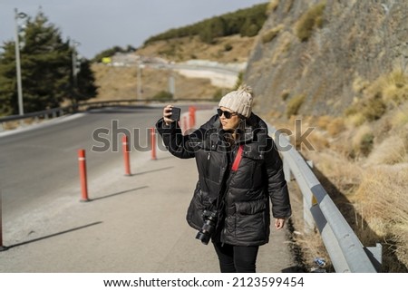 A shot of a Caucasian woman walking on a roadside and taking some pictures with the phone 