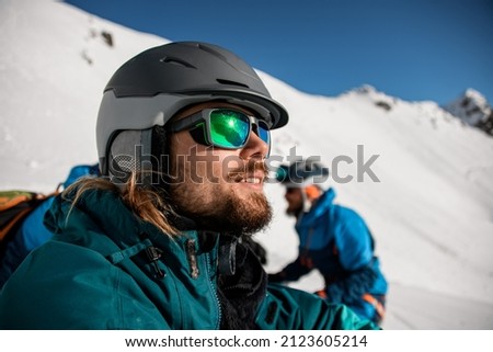 selective focus on the face of a bearded man in sunglasses and a ski helmet on the background of a snowy mountain