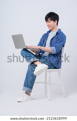 Young Asian man sitting and using laptop on white background Royalty-Free Stock Photo #2123618999