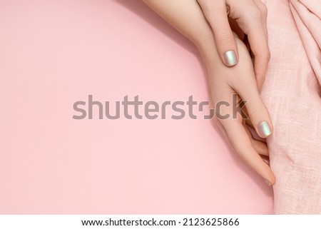 Female hands with glitter pearlescent nail design. Glitter pearlescent nail polish manicure. Female model hands with pink fabric on pink background. Copy space